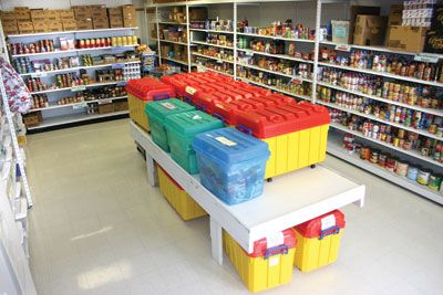 Shelves of tinned and packaged food in the pantry, with coloured bins of groceries ready for collection.